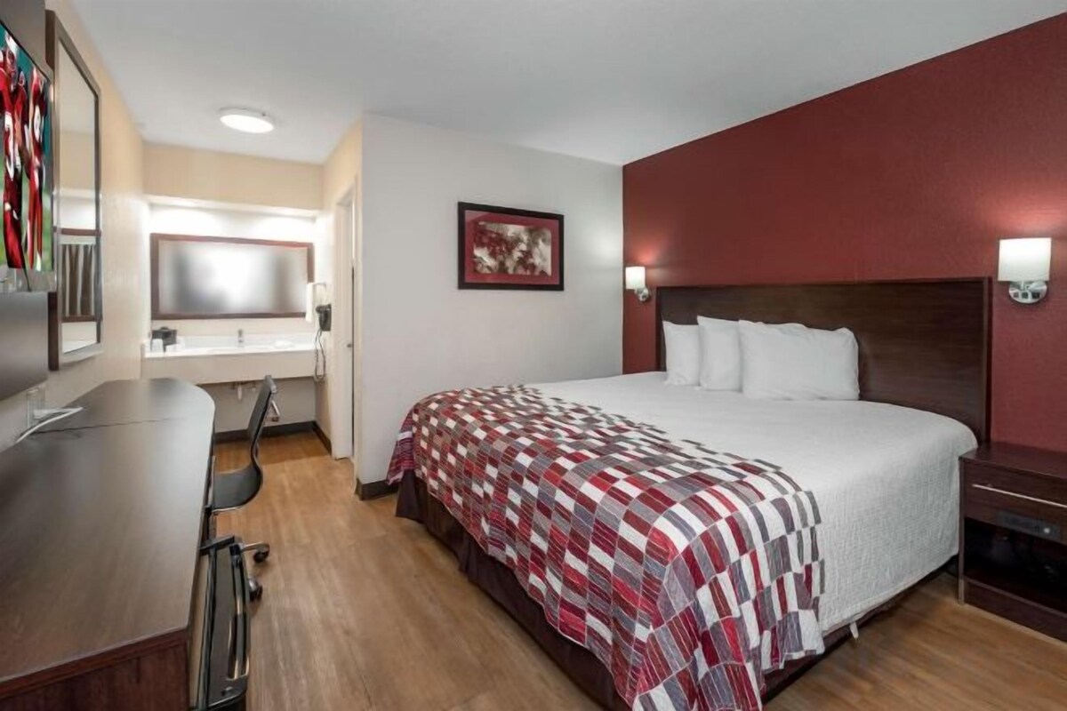 Habitación de hotel con cama, escritorio, silla, espejo y televisor en la pared.