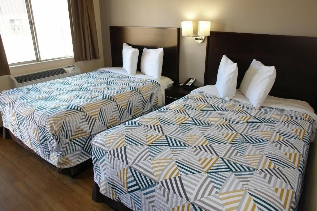 Two double beds with patterned bedding, a nightstand with a phone, and a wall-mounted light fixture.