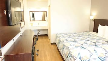 A hotel room with a bed, a desk, a chair, a TV, a mirror, and a nightstand.
