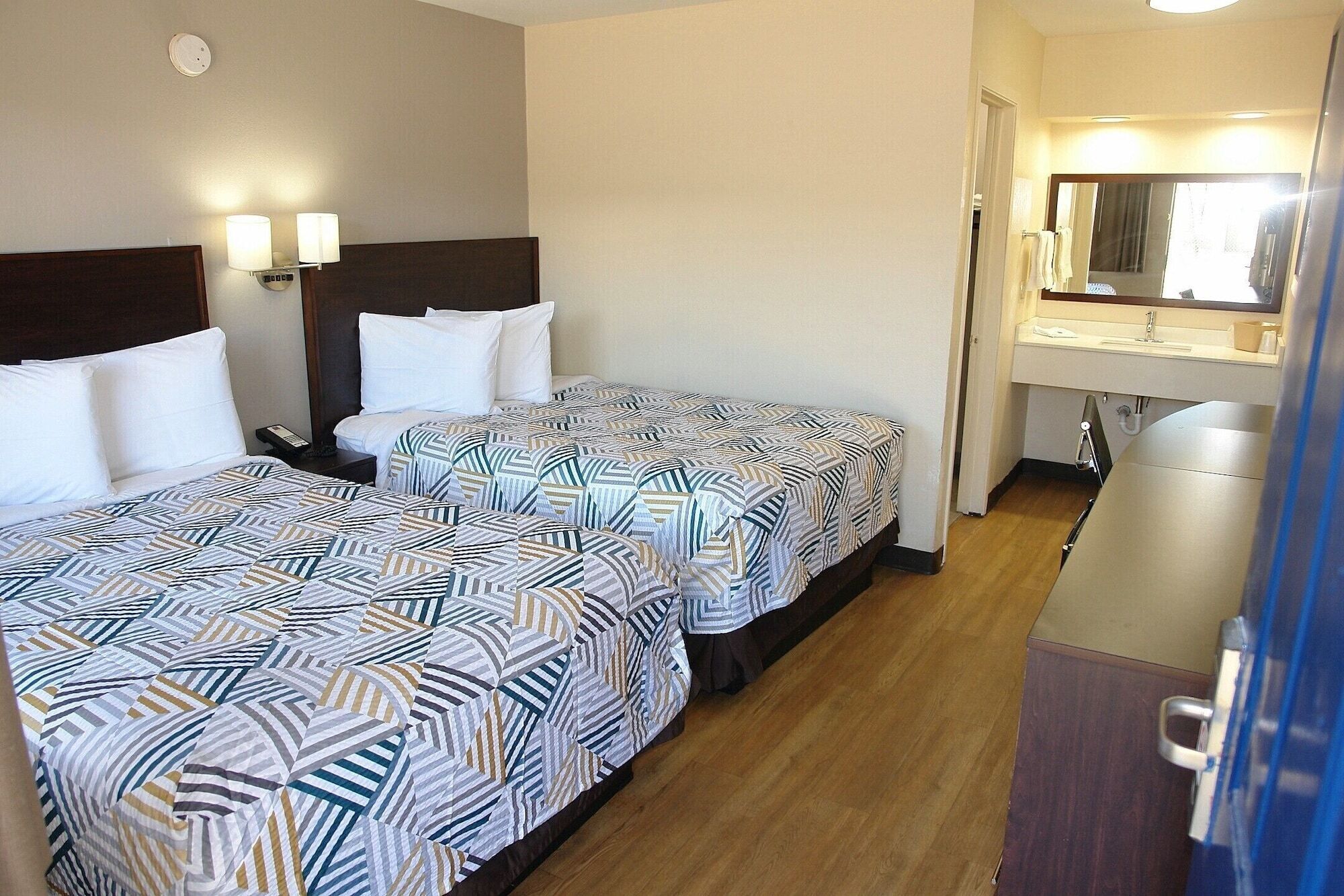 Une chambre d’hôtel avec deux lits, une salle de bain avec un miroir et un bureau.