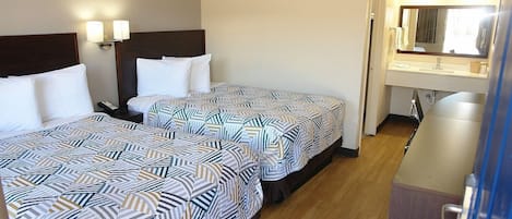 Une chambre d’hôtel avec deux lits, une salle de bain avec un miroir et un bureau.