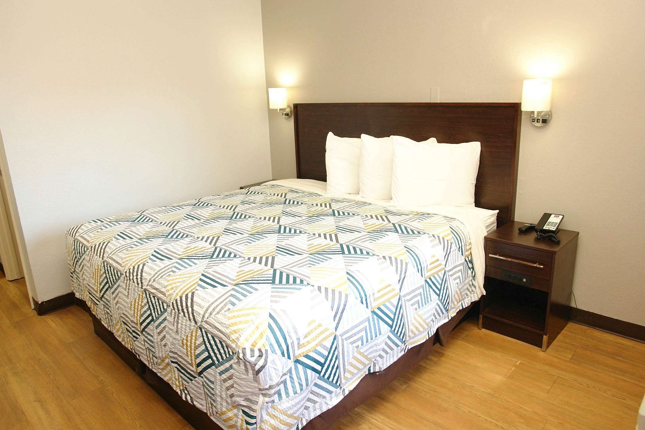 A neatly made bed with a patterned bedspread, a wooden headboard, two bedside lamps, and a small bedside table with a phone.