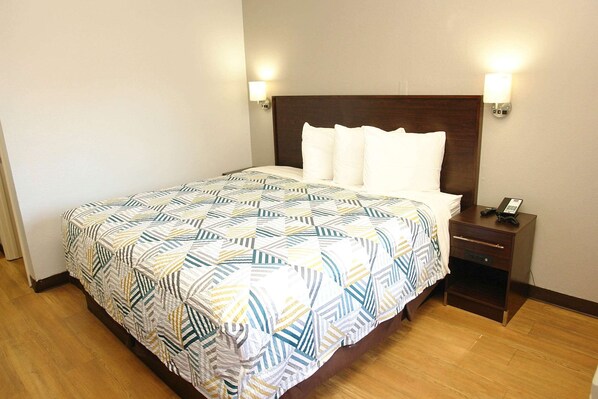 A neatly made bed with a patterned bedspread, a wooden headboard, two bedside lamps, and a small bedside table with a phone. - Motel 6 Hattiesburg, MS (Hattiesburg)