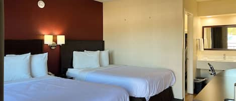 A hotel room with two beds, a nightstand, a wall-mounted lamp, a mirror, and a wooden floor.