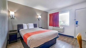 A hotel room with a bed, bedside tables, wall-mounted lamps, a window with curtains, an air conditioning unit, and a door with a lock. - Motel 6 Gallup, NM (Gallup)