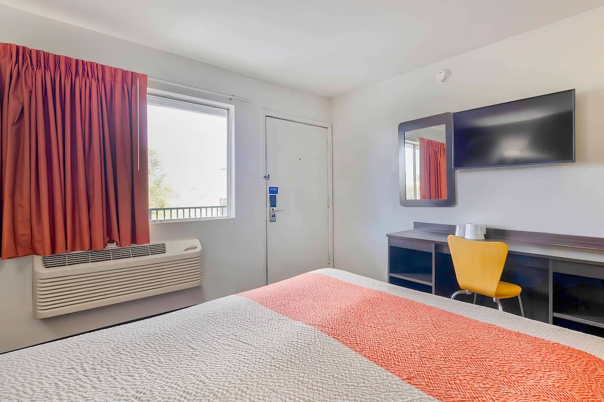 A hotel room with a bed, a desk, a chair, a TV, and a window with curtains.