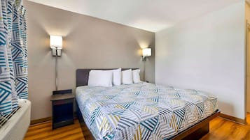 Una habitación de hotel con una cama, mesitas de noche, un calentador y dos lámparas fijadas a la pared.