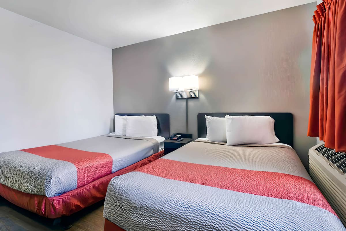 Habitación de hotel con dos camas, una mesita de noche, una lámpara y un equipo de aire acondicionado.