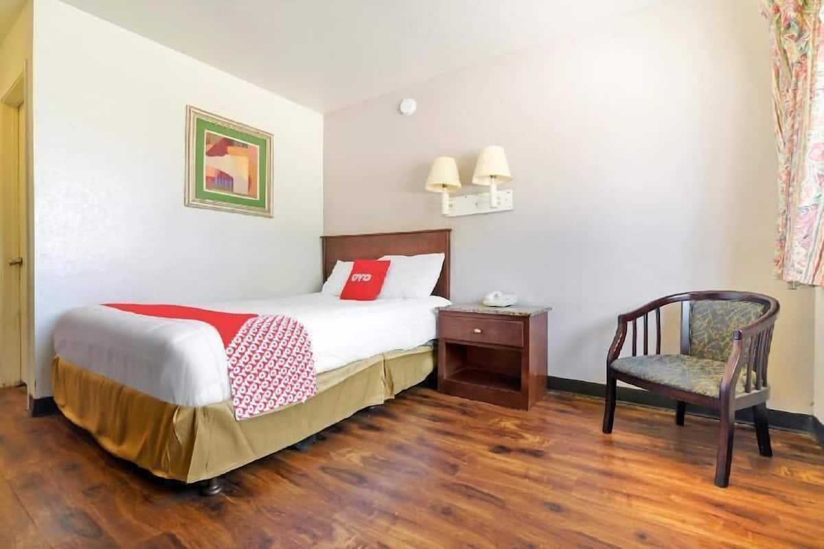 A hotel room with a bed, bedside table, chair, and a wall-mounted lamp.