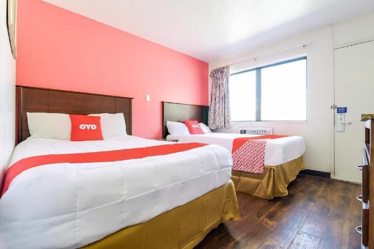 Two beds with white and red bedding, a window with curtains, and a wooden floor.