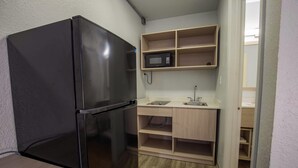 Eine kleine Küche mit einem schwarzen Kühlschrank, einer Mikrowelle und Holzregalen.