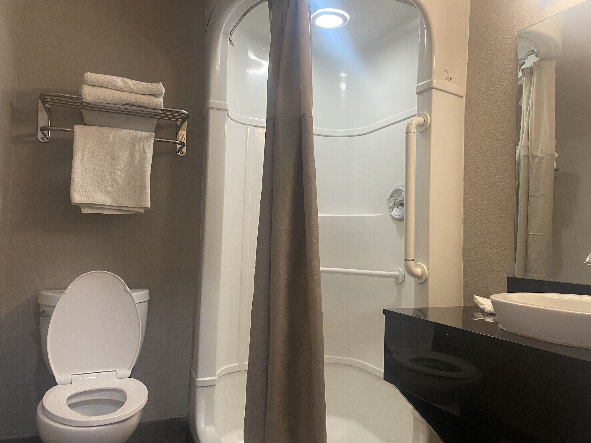 Et badeværelse med toilet, bruseniche, håndvask og håndklædestige.