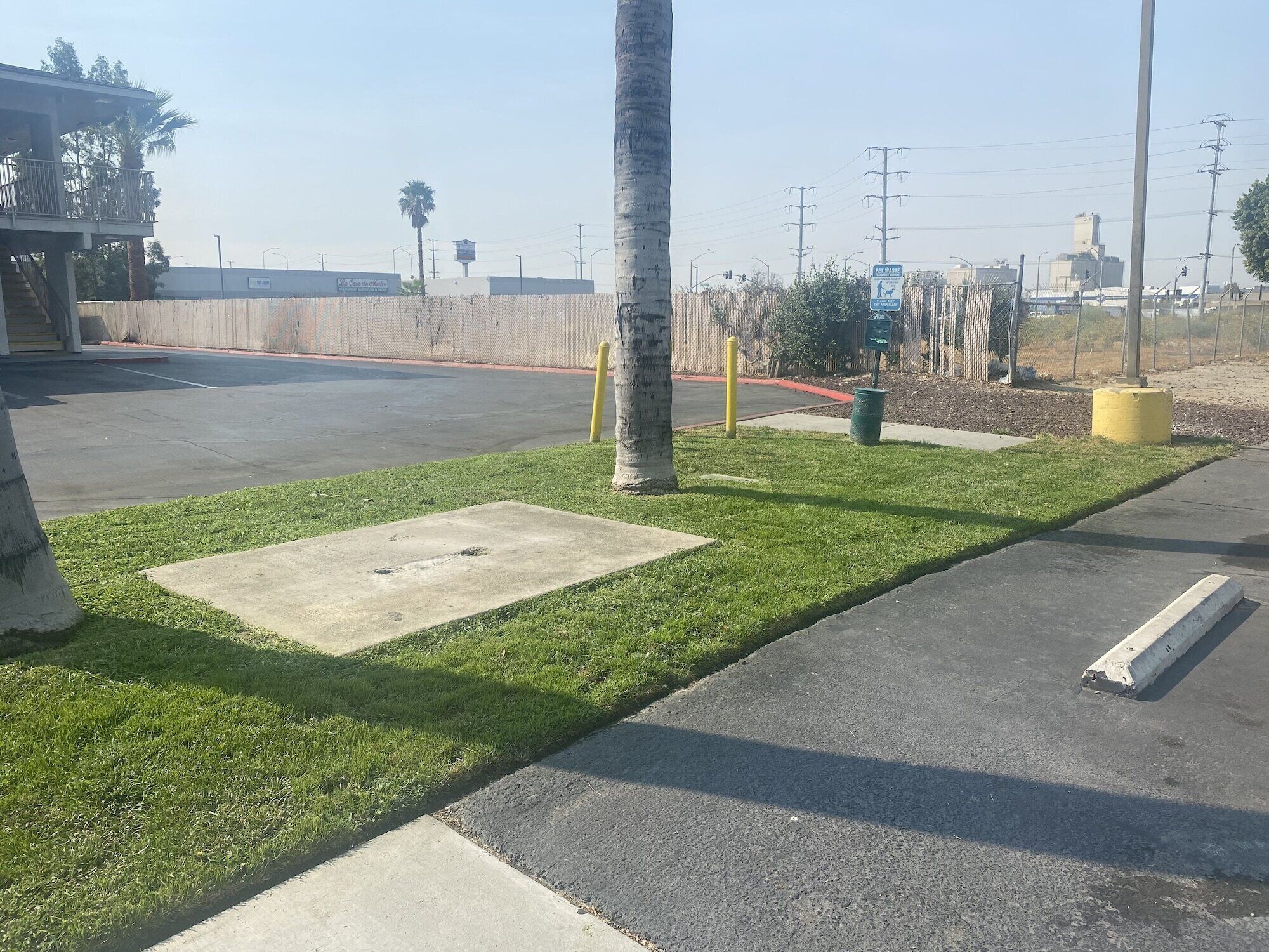 Un estacionamiento con zona verde, superficie de hormigón y un bolardo amarillo.