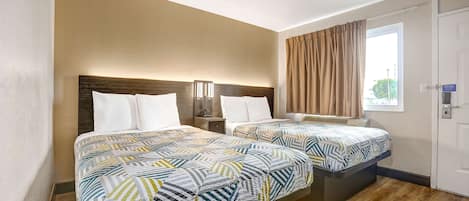 Habitación de hotel con dos camas, cada una con una colcha estampada, una mesita de noche con lámpara y un ventanal con cortinas.
