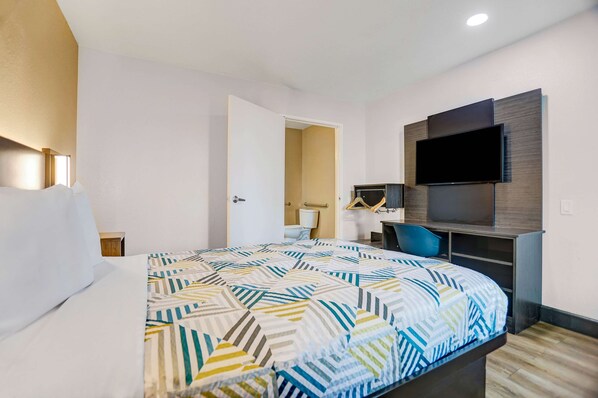 Een hotelkamer met een groot bed, een bureau met stoel, een flatscreen televisie aan de muur en een deur naar de badkamer.