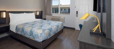 A hotel room with a bed, a desk, a chair, a TV, and a window with a view of buildings.