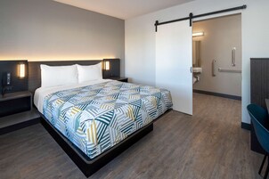 Una habitación de hotel moderna con una cama grande, mesitas de noche, un escritorio y un baño visible a través de una puerta abierta.