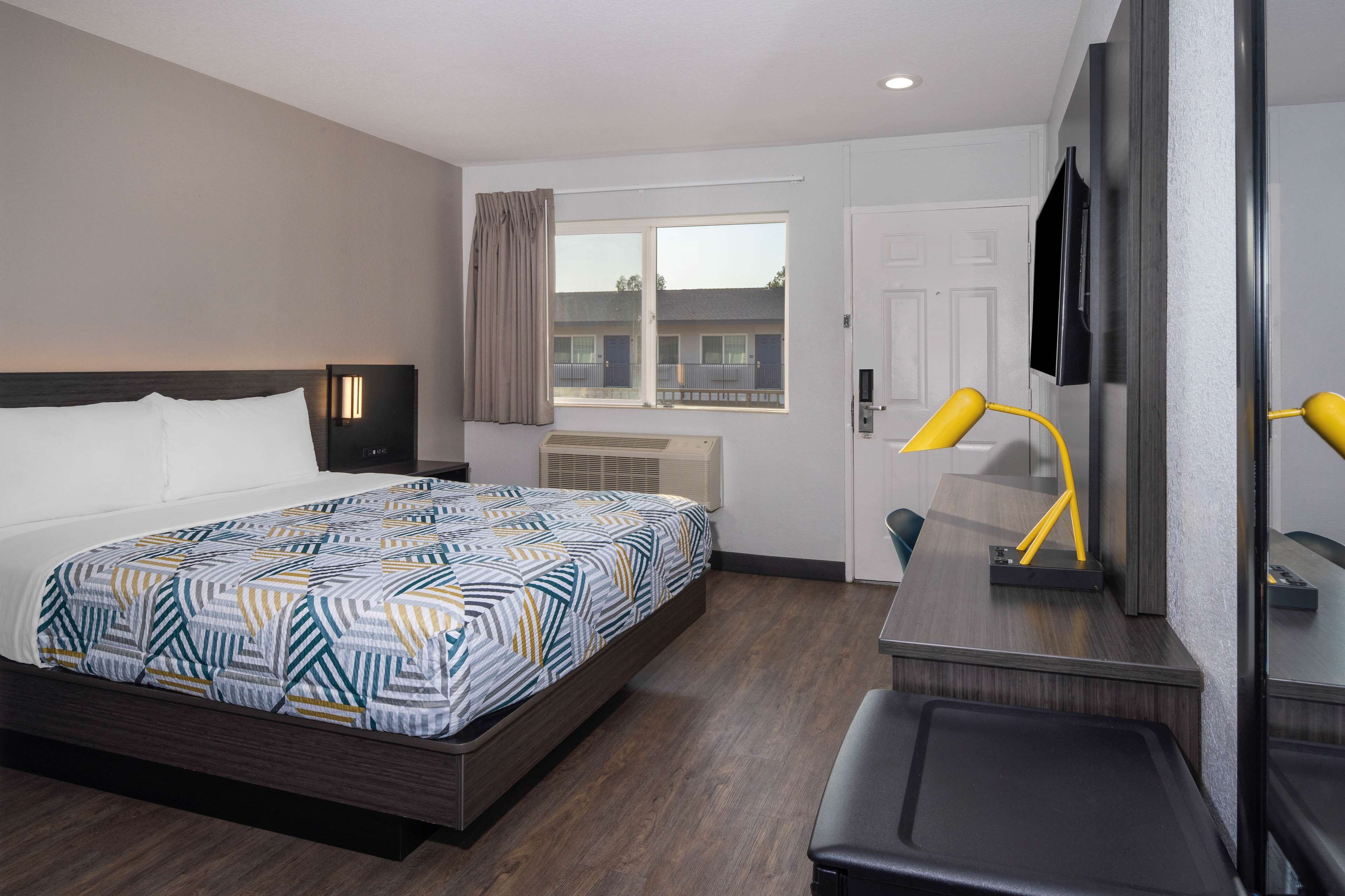 A hotel room with a bed, a desk, a chair, a TV, and a window with curtains.
