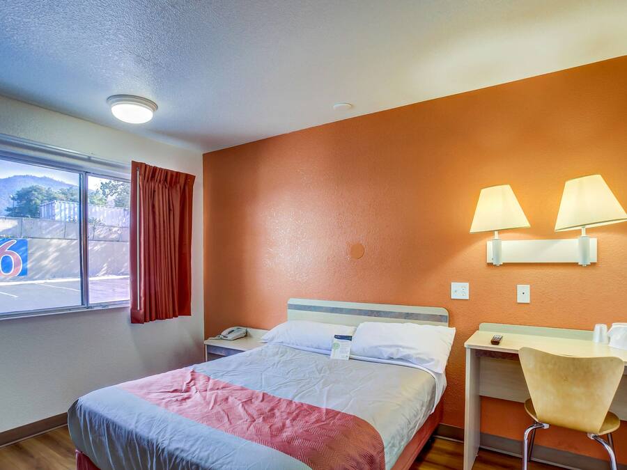 Una habitación de hotel con cama, escritorio, dos lámparas, una silla y ventana con cortinas.