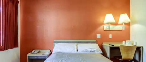 Habitación de hotel con cama, escritorio, silla, teléfono y dos lámparas fijadas a la pared.