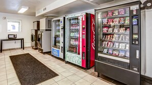 A vending area with various beverage machines, including Coca-Cola and Aquafina water dispensers, and a microwave on a table. - Motel 6 Grants Pass, OR (Grants Pass)