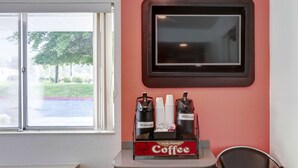 A coffee station with a red wall, a window with a view of trees, and a framed picture above it. - Motel 6 Grants Pass, OR (Grants Pass)