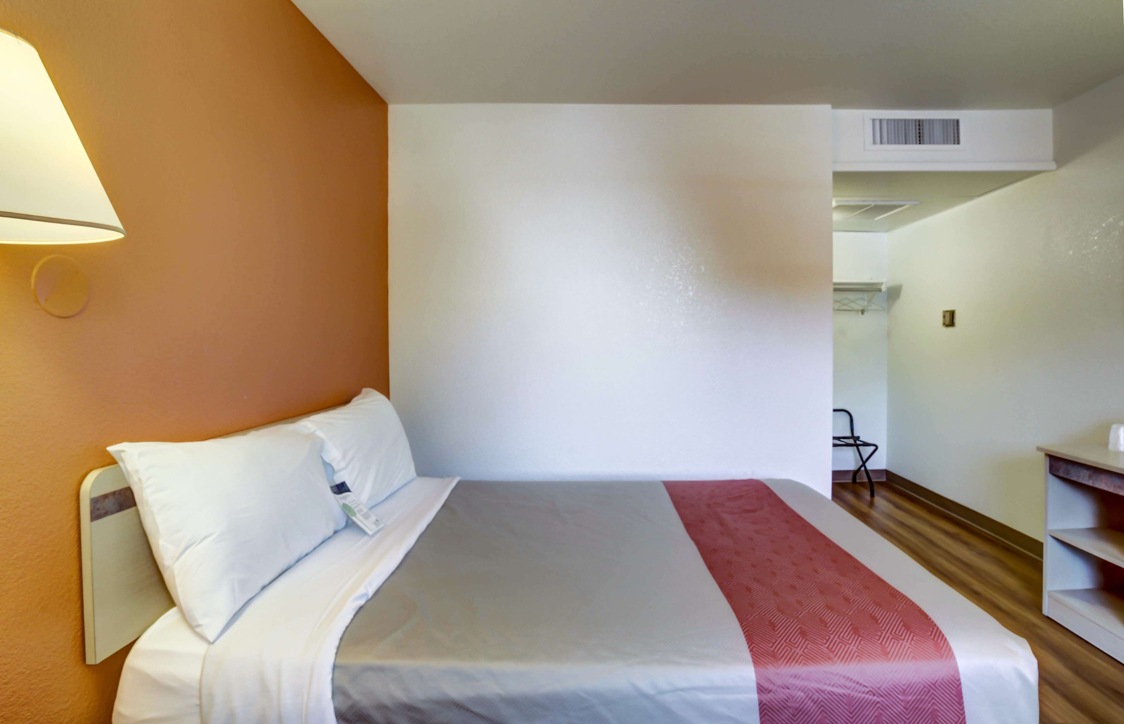 Una habitación de hotel con una cama, una mesita de noche, una lámpara y una silla.