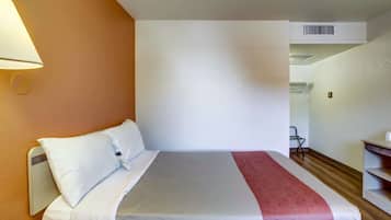 Una habitación de hotel con una cama, una mesita de noche, una lámpara y una silla.