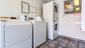 A laundry room with two front-loading washers and dryers, a digital scale, and a framed instruction manual on the wall.