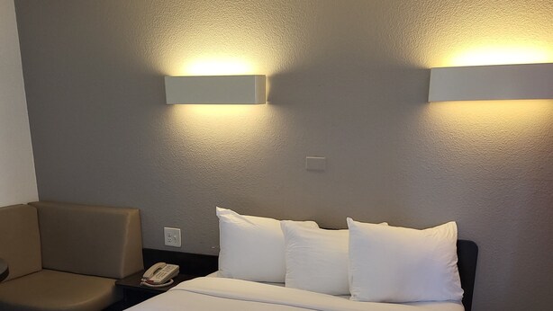 A hotel room with a large bed, two bedside tables, a chair, and two wall-mounted light fixtures.