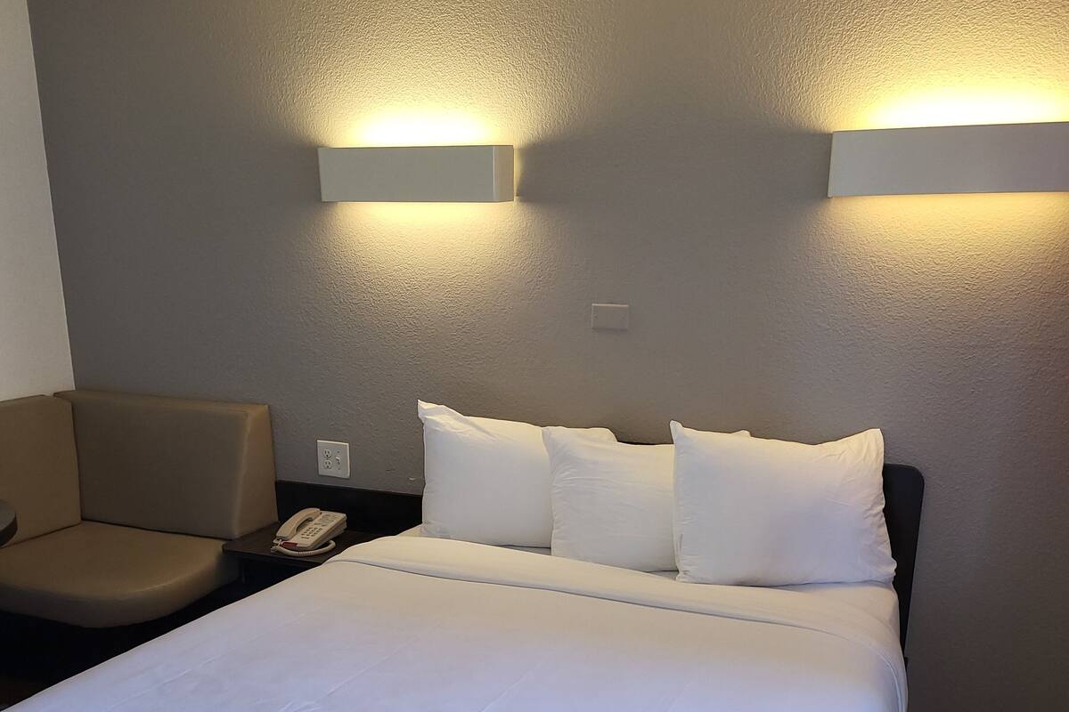 A hotel room with a large bed, two bedside tables, a chair, and two wall-mounted light fixtures.