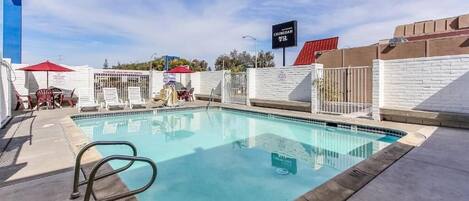A swimming pool with a metal ladder, surrounded by a white fence and a red umbrella.