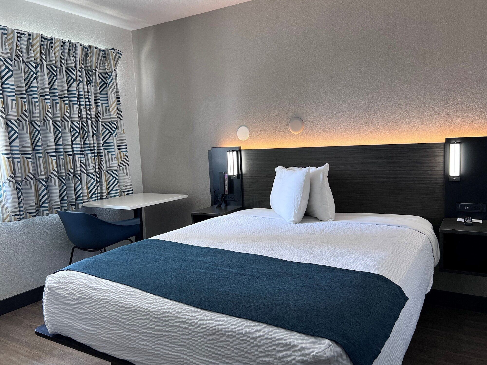 A modern hotel room with a large bed, a desk, and a chair.