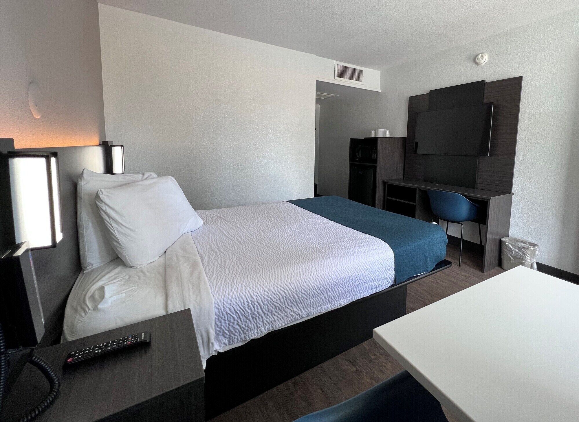 A hotel room with a bed, a desk, a chair, a TV, and a phone.