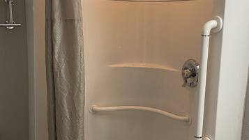 Une douche d’angle avec une porte en verre, un pommeau de douche et une barre d’appui.