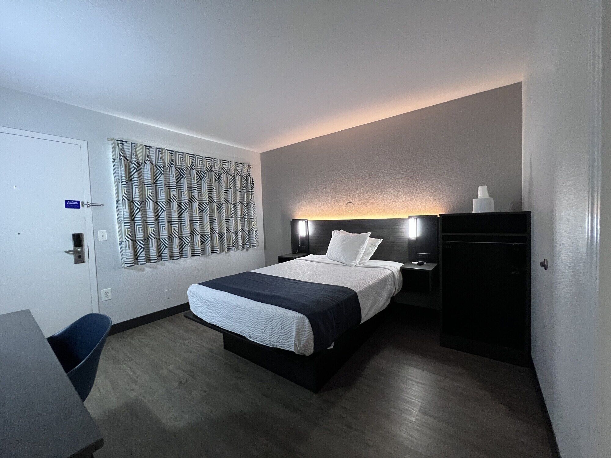 A hotel room with a bed, a desk, a wardrobe, and a patterned wall.