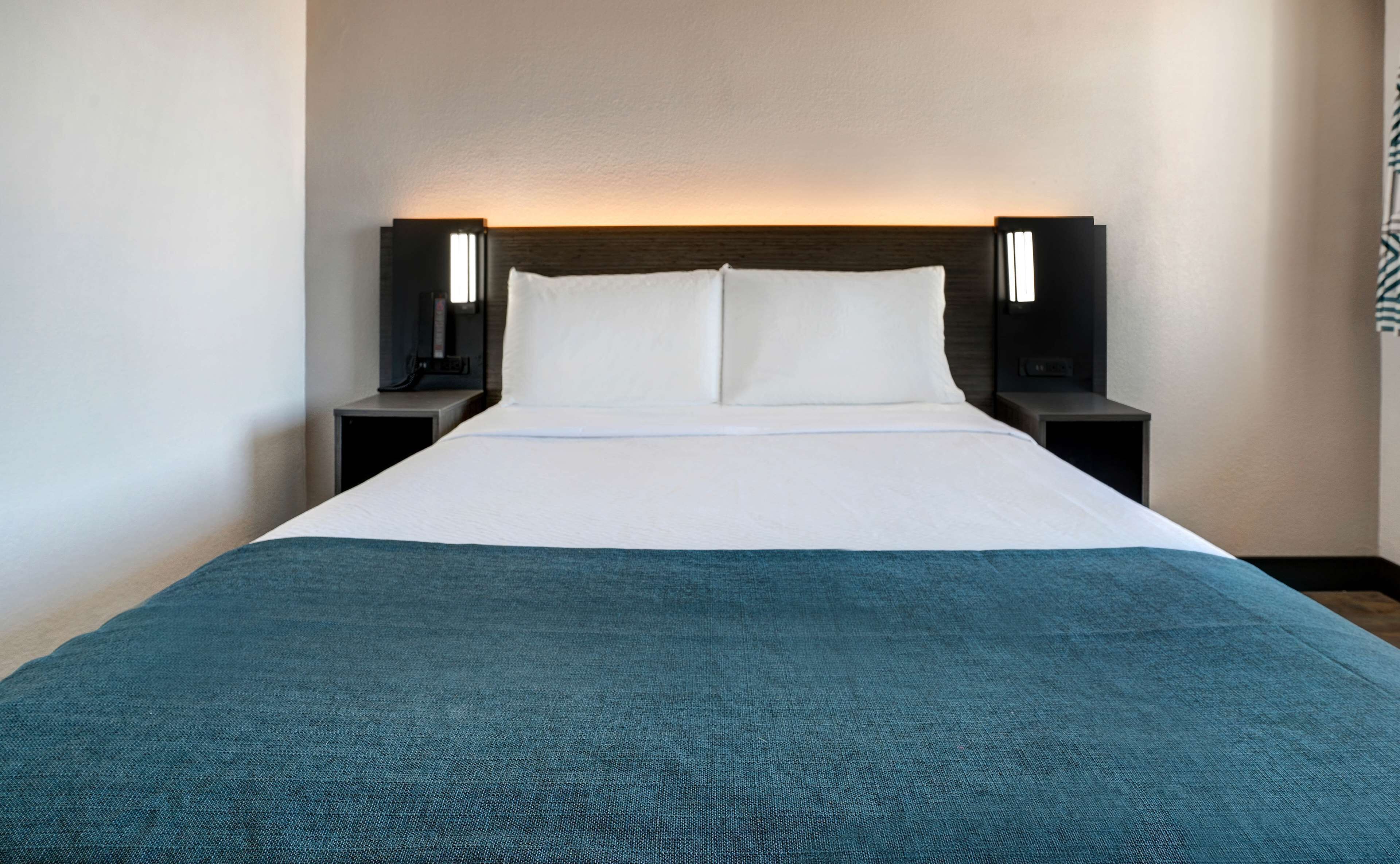 A hotel room with a large bed, two bedside tables, and a headboard with integrated lighting.