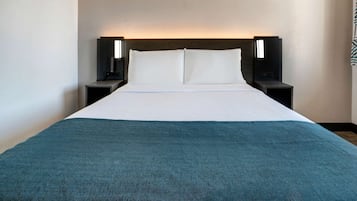 A hotel room with a large bed, two bedside tables, and a headboard with integrated lighting.