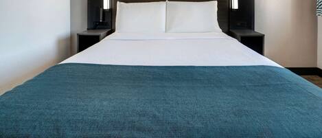 A hotel room with a large bed, two bedside tables, and a headboard with integrated lighting.