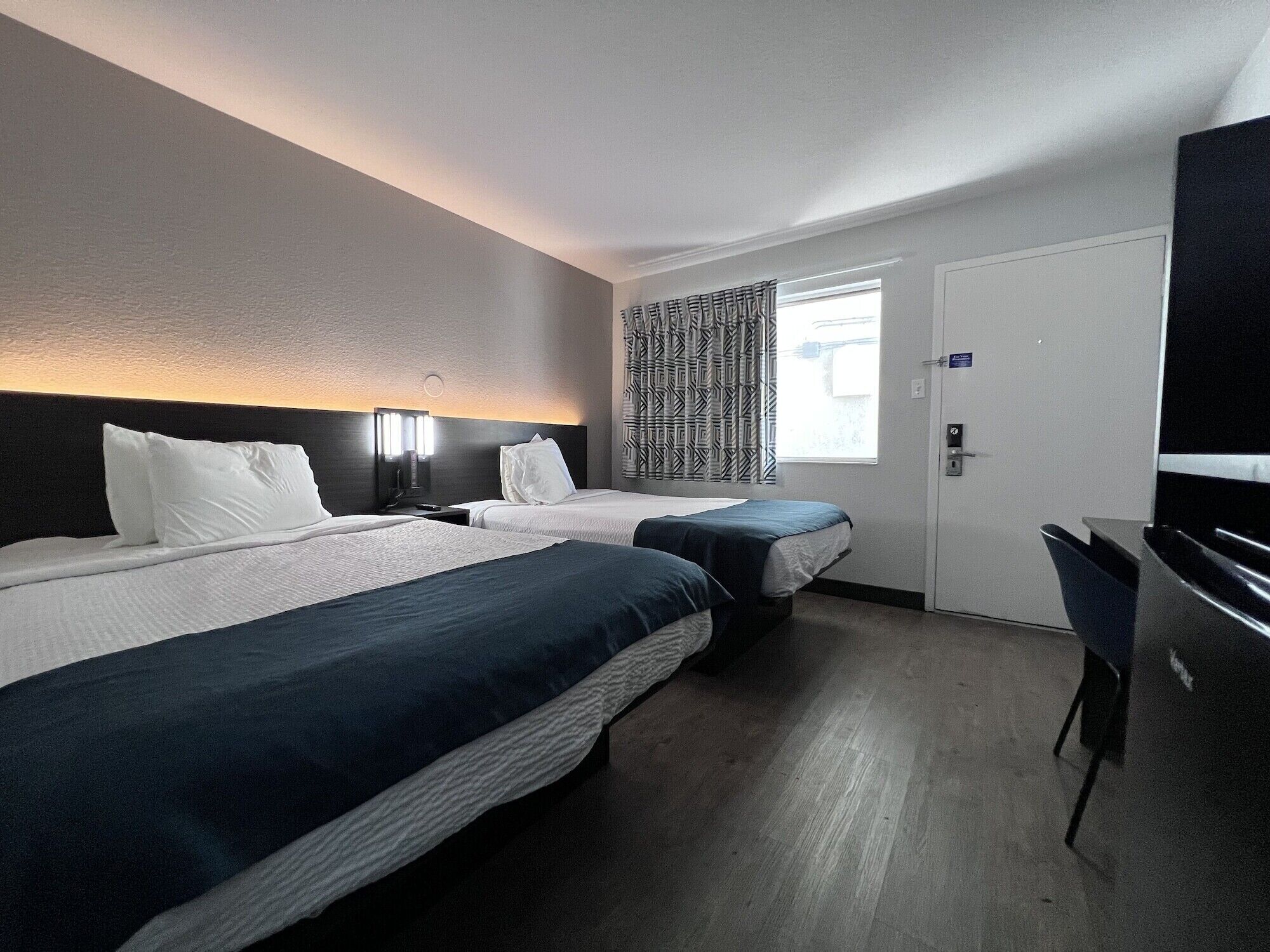 A hotel room with two beds, a desk, and a door.