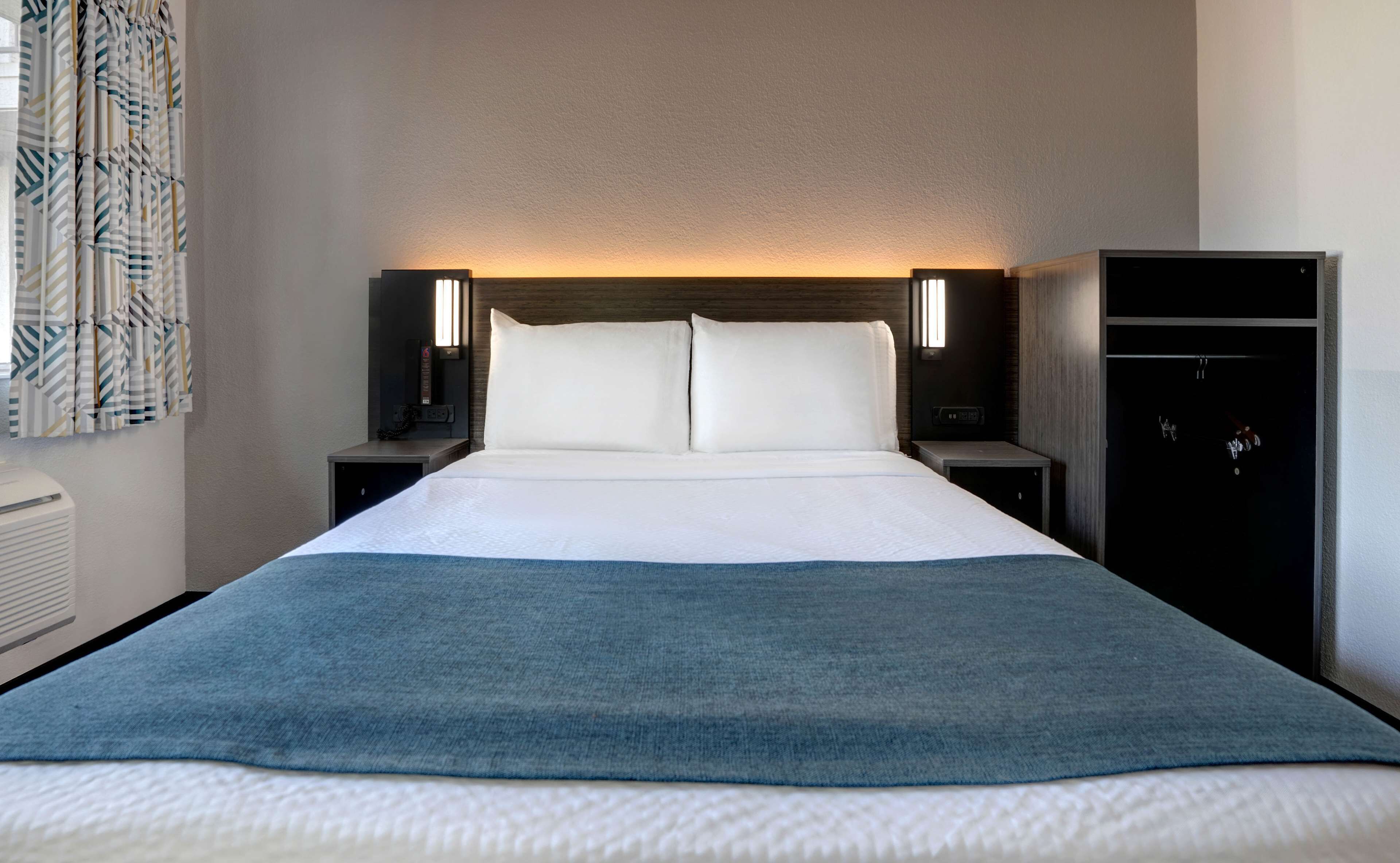 Une chambre d’hôtel avec un grand lit, deux tables de chevet avec des lampes, une armoire et un rideau à motifs.