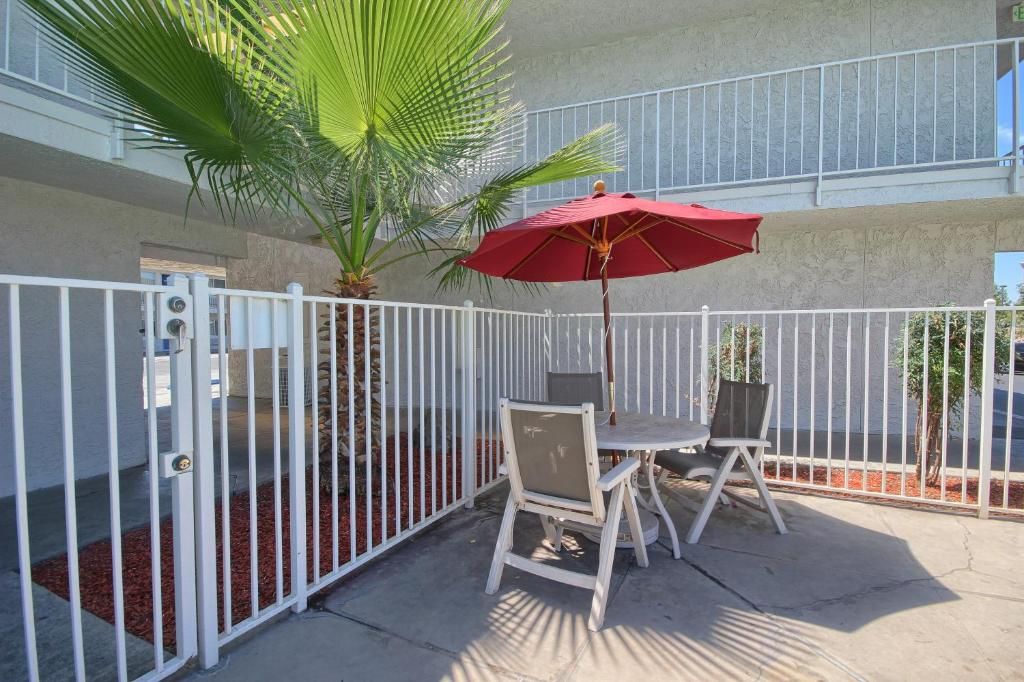 A gated outdoor area with a table and chairs, a red umbrella, and a palm tree.