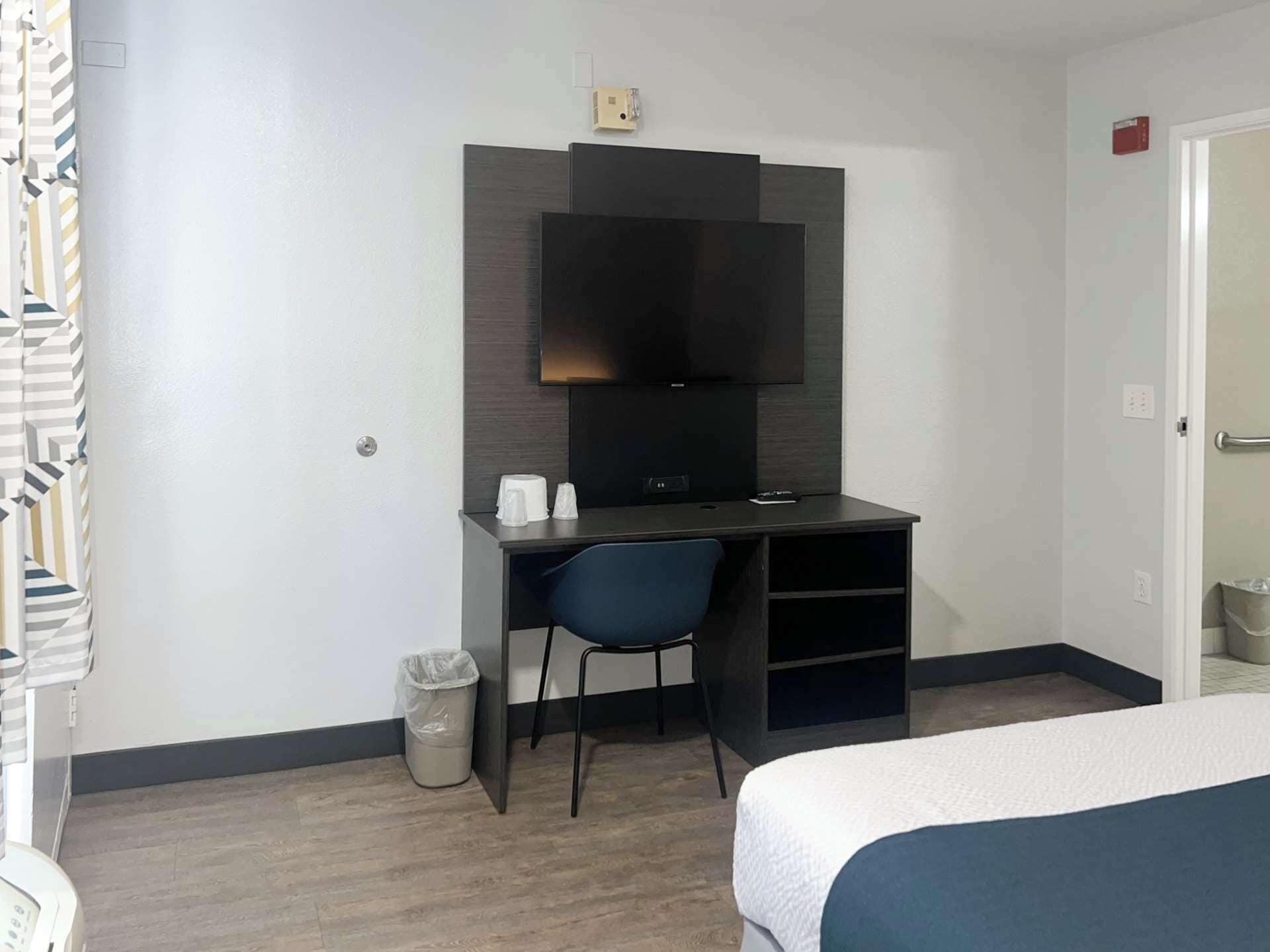 Une chambre d’hôtel comprenant un lit, un bureau avec une chaise, une télévision et une poubelle.