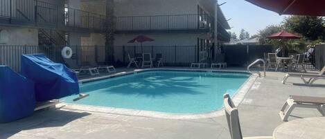 A rectangular swimming pool with a tiled deck, surrounded by lounge chairs and umbrellas.