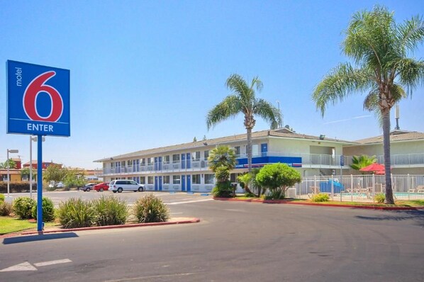 A motel with a clear entrance sign, a parking lot, and a building with multiple floors and balconies. - Motel 6 Tulare, CA (Tulare)