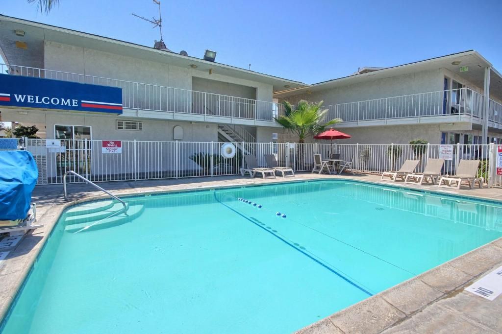 A hotel with a swimming pool, a 'WELCOME' sign, and a fenced area with lounge chairs.