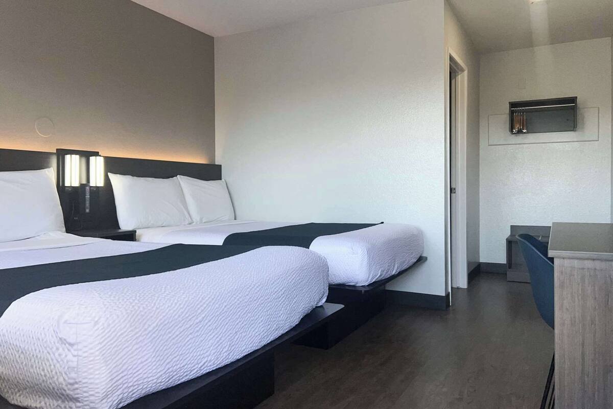 Una habitación de hotel con dos camas, un escritorio y un televisor en la pared.
