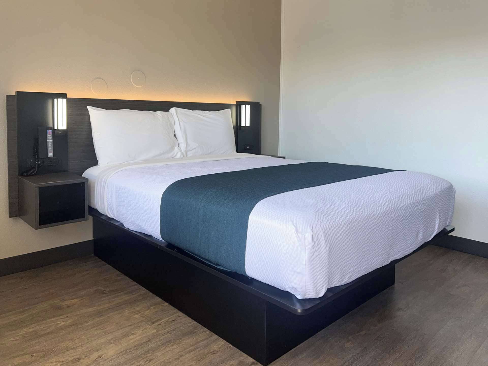 A modern hotel room with a large bed, a bedside table, and a wall-mounted light fixture.
