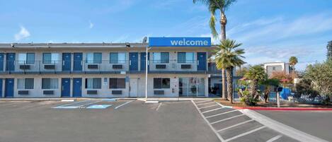 Un motel con un letrero de 'welcome', varias habitaciones y un estacionamiento.