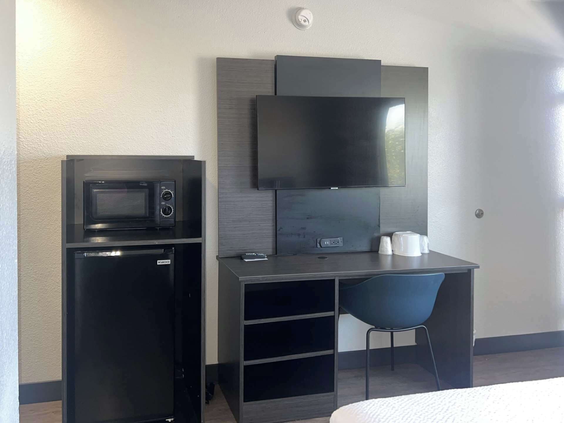 Une chambre d’hôtel compacte dotée d’une kitchenette, d’un téléviseur à écran plat, d’un petit bureau et d’une chaise.